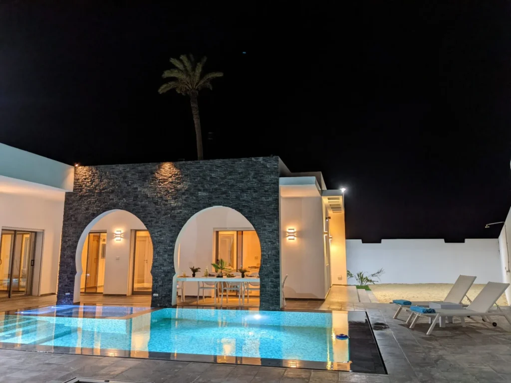 Terrasse de la villa Diamant, à Ethic Village Djerba : arches en pierre noire, table dressée et piscine éclairée en soirée