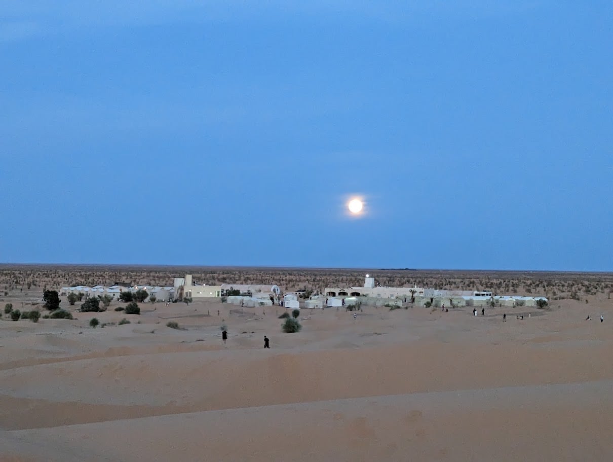 Oasis de Ksar Ghilane au crépuscule avec pleine lune au-dessus des palmiers