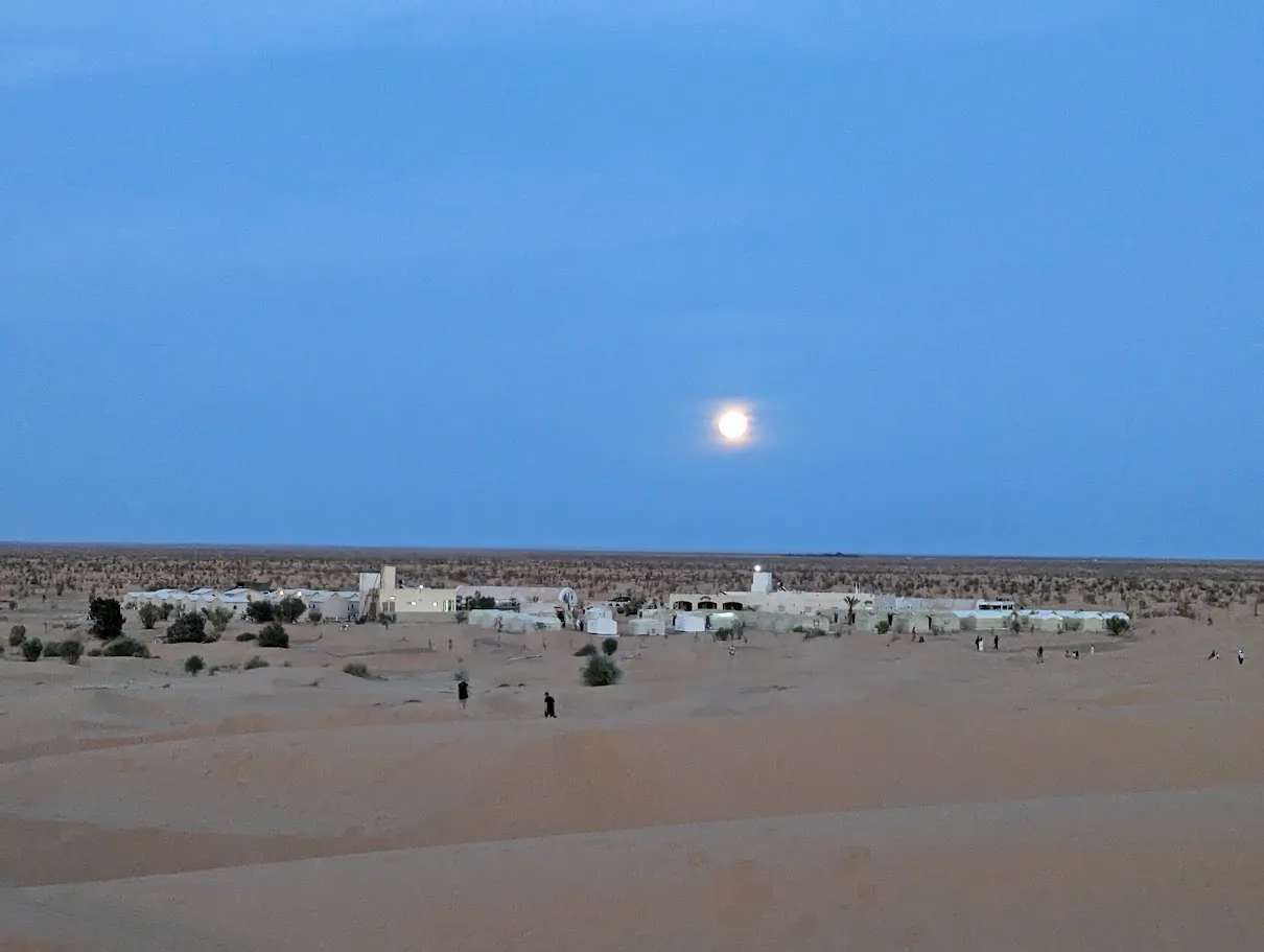 Oasis de Ksar Ghilane au crépuscule avec pleine lune au-dessus des palmiers