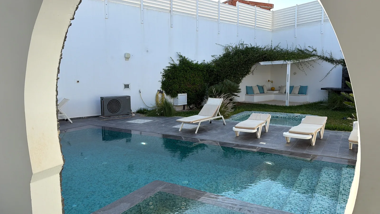 Villa Diamant, a piscina vista do arco, em outubro Piscina privada da villa Diamant em Djerba em outubro, vista através de um arco branco, com espreguiçadeiras e mosaico turquesa