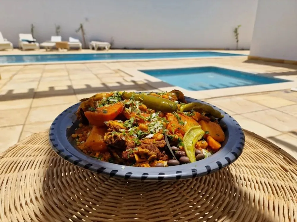 Cuscuz tunisino à beira da piscina Cuscuz tunisino com carne e legumes, azeitonas e malaguetas, servido numa mesa de vime à beira de uma piscina da residência