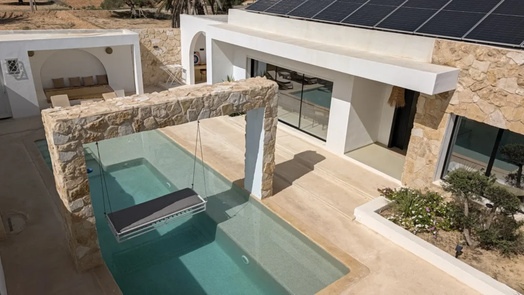 Villa Opale at Ethic Village Djerba seen from above: private pool with a hanging swing under a stone arch, white façade and solar panels on the roof