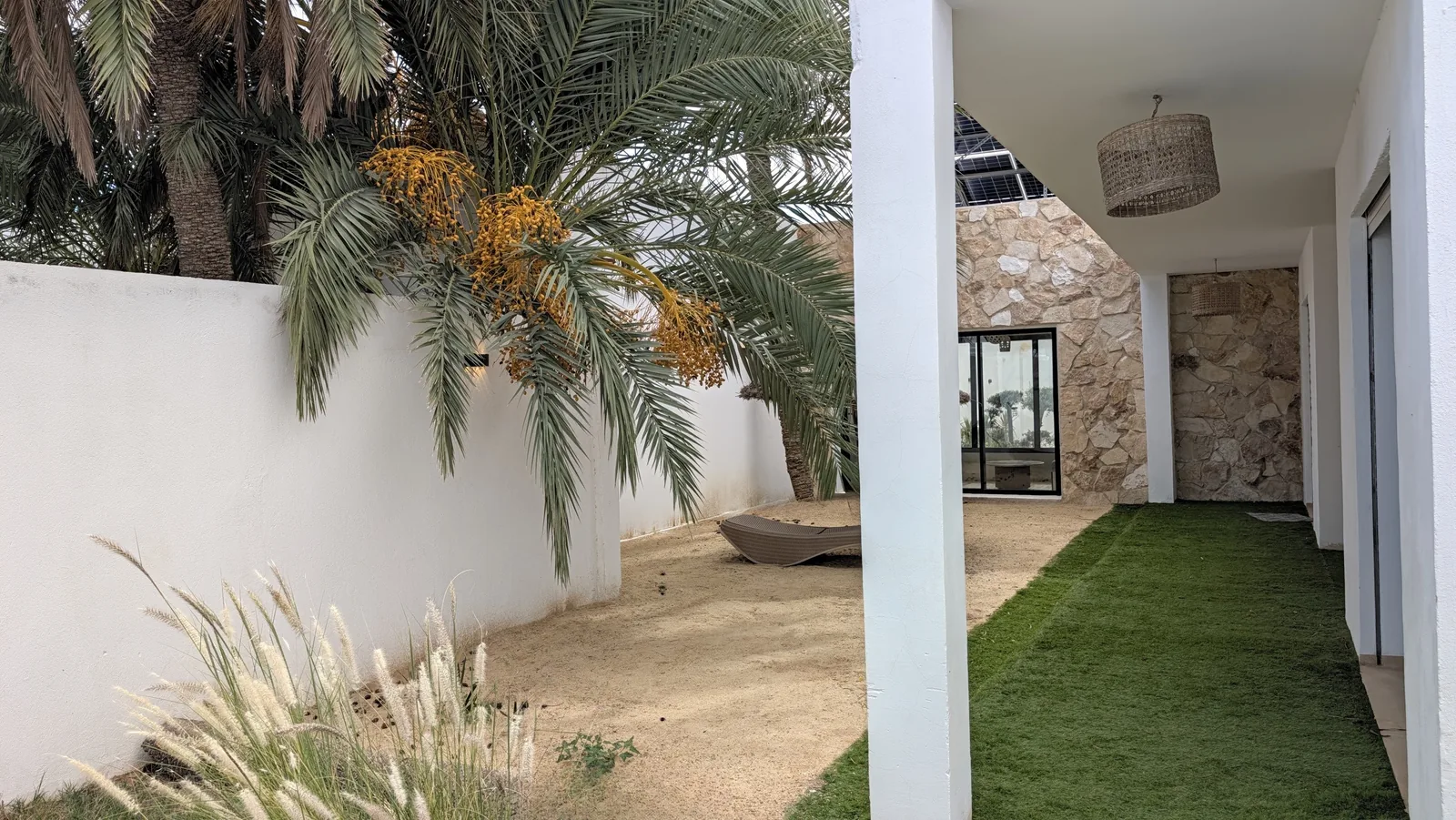 Giardino sabbioso della villa Opale a Djerba: palma da dattero carica di datteri, sdraio e porticato con pilastri bianchi